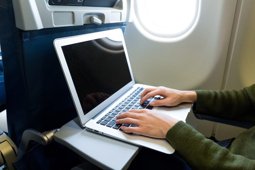 A Travel writer works on their laptop on a plane